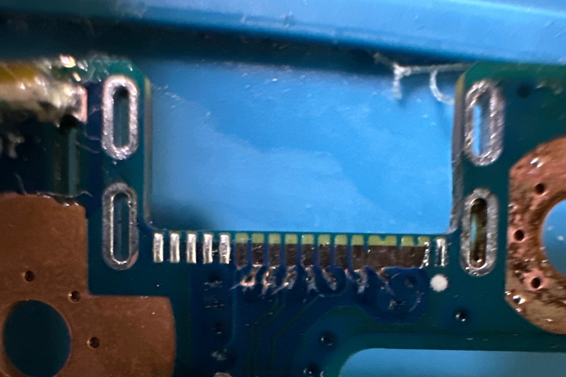 Damaged connector area before repair, with the port removed and lifted pads visible
