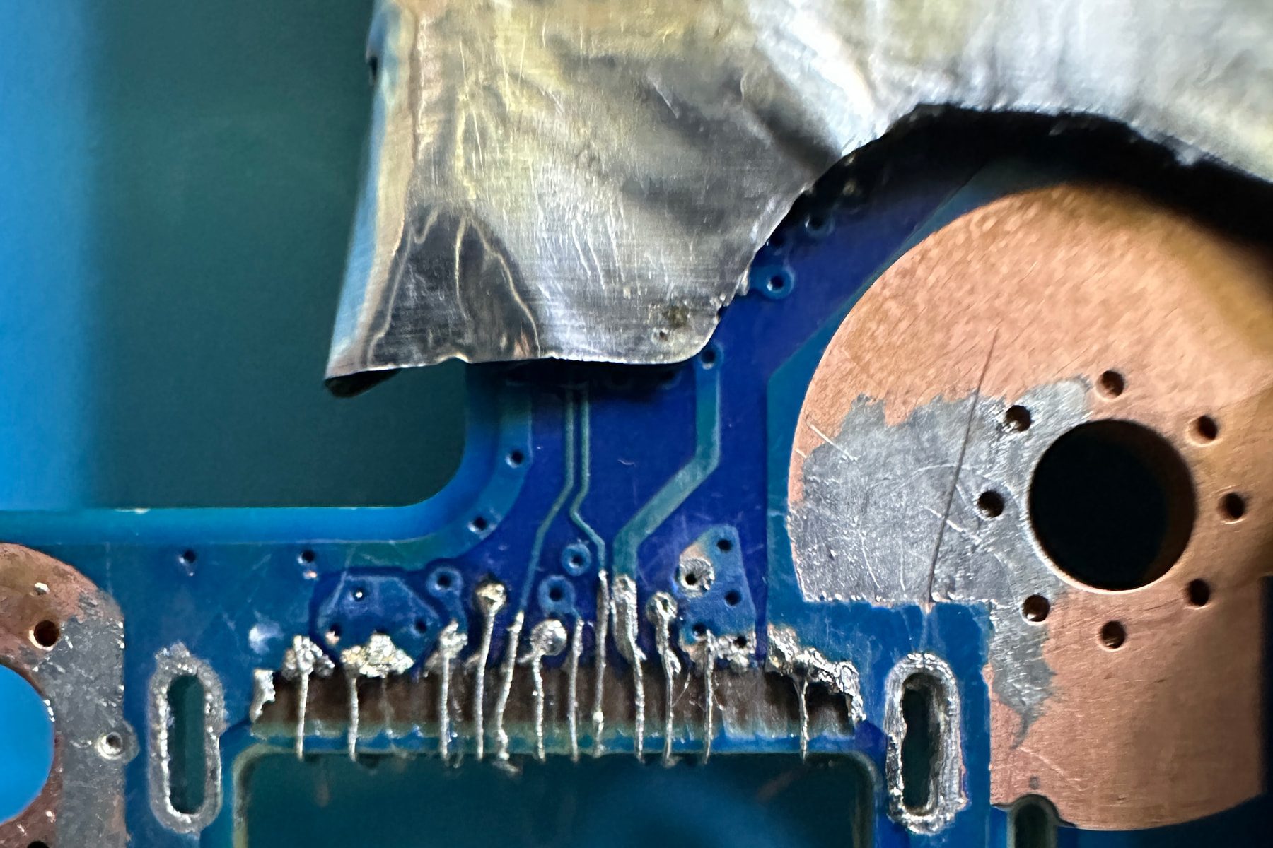 Close-up from the repair bench showing reconstructed copper pads and fine jumper wires at a damaged connector area
